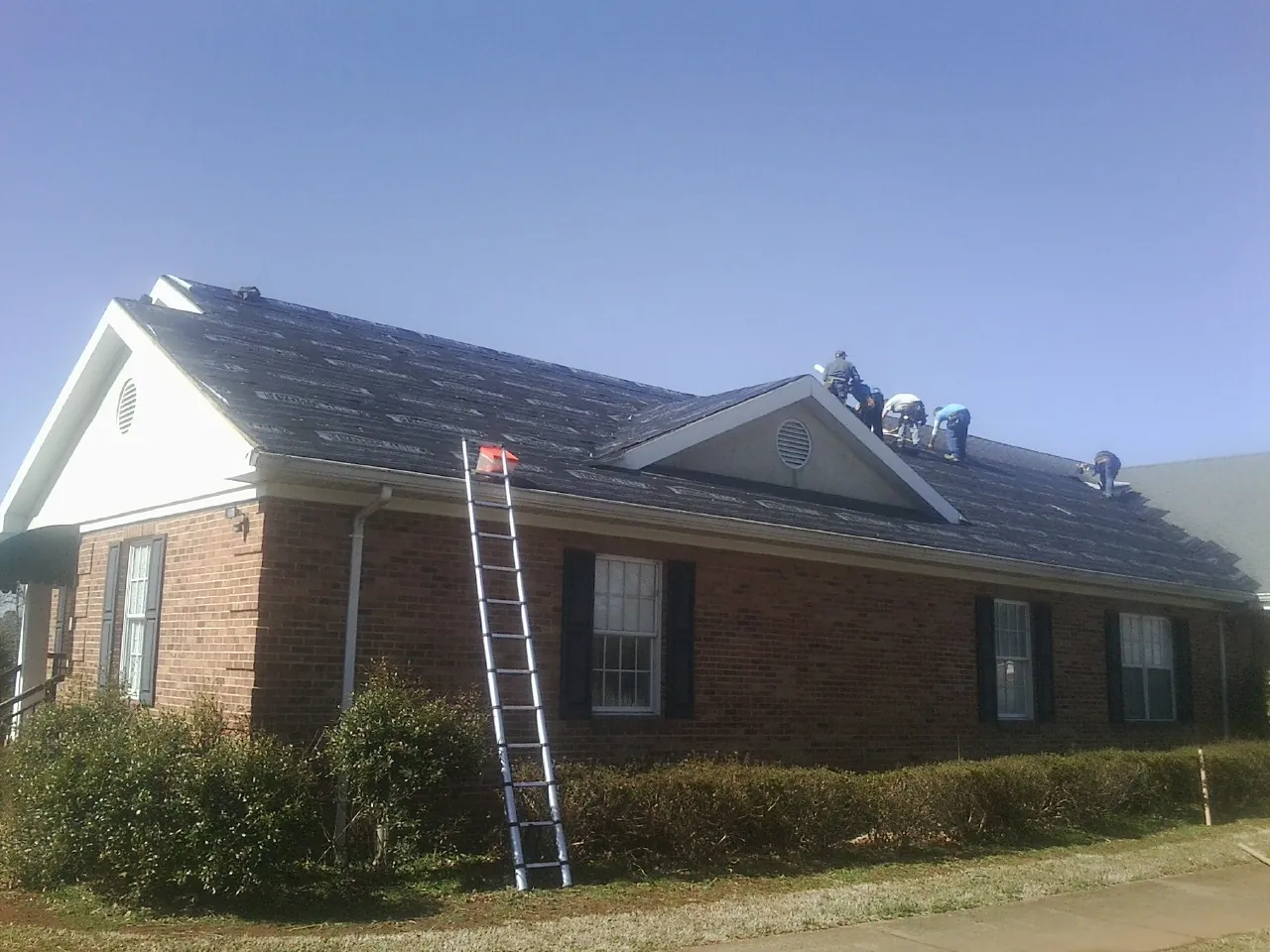 Crew tearing shingles off a brick ranch roof with a ladder set — Metal Roof Repair work by our crew in Cragsmoor