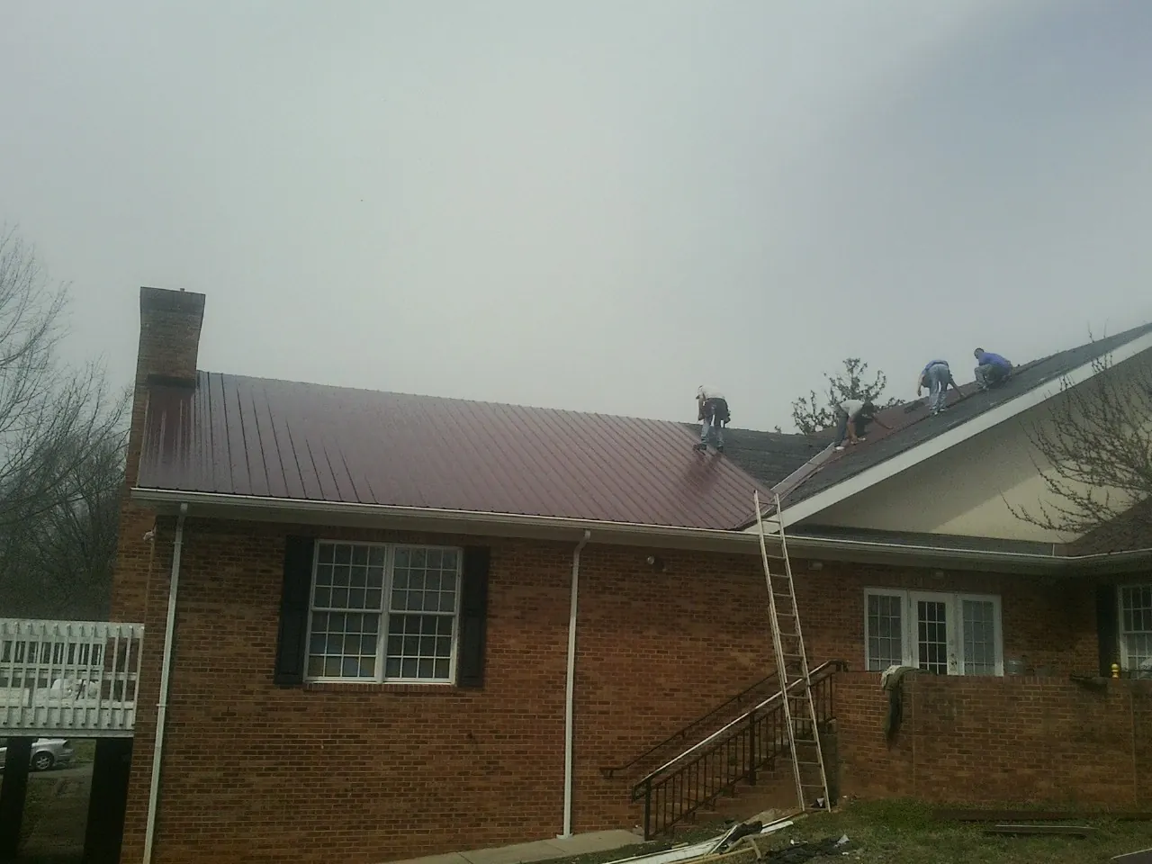 Crew setting red metal roofing panels on a brick home in Cragsmoor