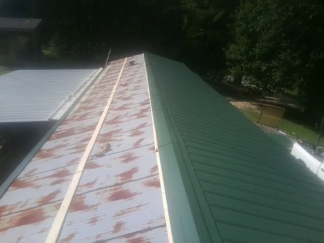 Old rusted panels beside newly installed green metal roofing — Wind Damage Roof Repair by Roofing Brothers in Cragsmoor