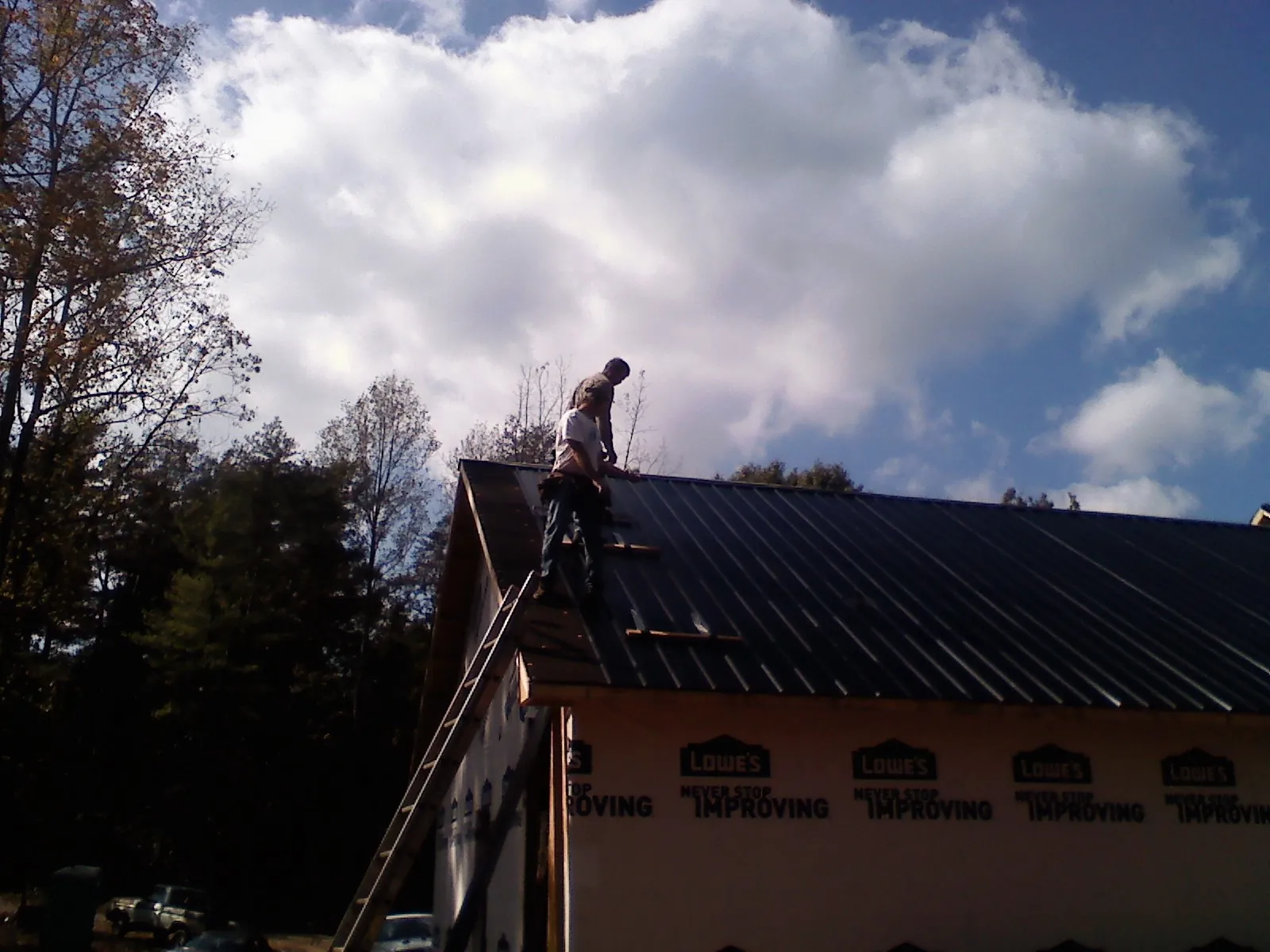 Roofer fastening dark metal panels high against a cloudy sky, from a Roof Inspection job in Cragsmoor