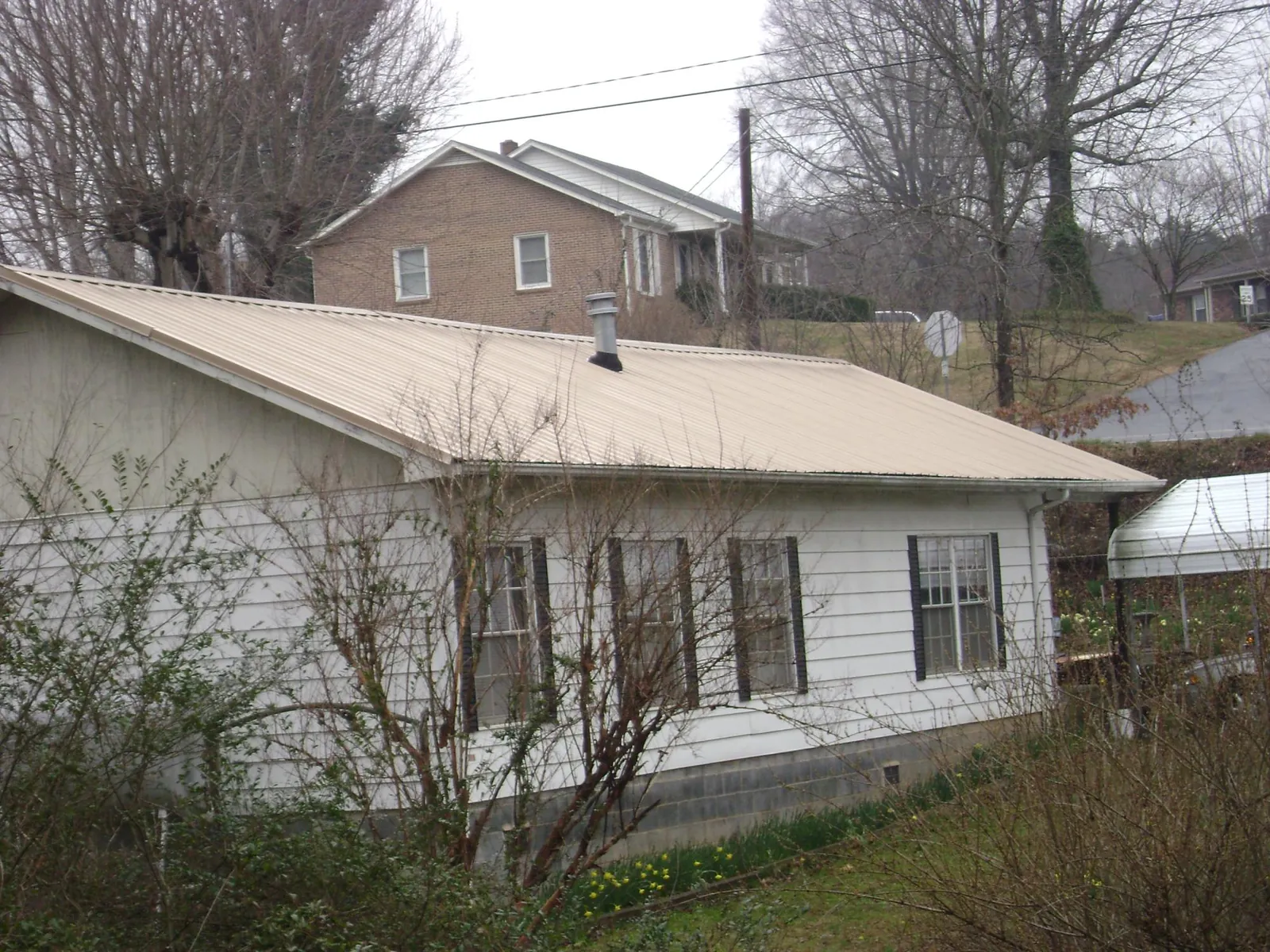 Tan metal roof on a white sided house set into a hillside — Commercial Roofing by Roofing Brothers in Cragsmoor